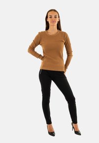 Maglione a maniche lunghe marrone a coste con collo rotondo e bottoni sulle spalle, abbinato a pantaloni neri slim-fit e tacchi neri a punta.