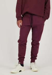Bordeaux joggers met een slim fit, gemaakt van zachte stof. Voorzien van een elastische tailleband met trekkoord en geribde boorden. Vergezeld van witte sneakers.