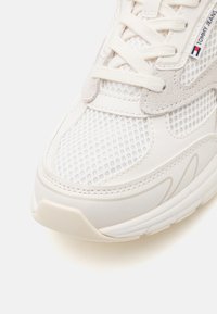 Hvit sneakers med nettingoverdel, semskede detaljer og teksturert gummisåle. Skolisser i matchende farge, med merketag på siden.