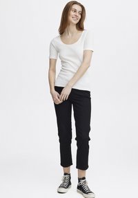 Top scurt alb cu model striat, cu decolteu rotund, asortat cu pantaloni negri până la gleznă și teniși negri cu guler înalt. Design simplu, ajustat.