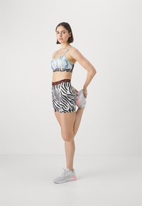 Top corto sporty con motivo ad acquerello blu, pantaloni corti a zebre con vita arancione e sneakers grigie chiare con accenti rosa.