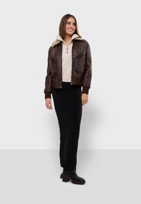 Veste aviateur en cuir marron avec un col en polaire beige, fermeture éclair à l'avant, deux poches poitrine, jupe noire et bottines.