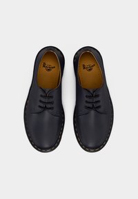 Tamsiai mėlyni odiniai oksfordų batai su apvaliais pirštais, pasižymintys lygiu paviršiumi, juodais raišteliais ir geltonais siūlais palei pado kraštą.