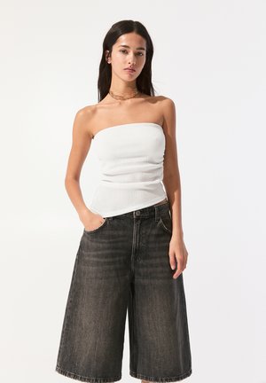 Witte geribbelde strapless top gecombineerd met hoge taille, brede denimbroek met een donkerblaue tint, subtiele textuur en voorzakken.