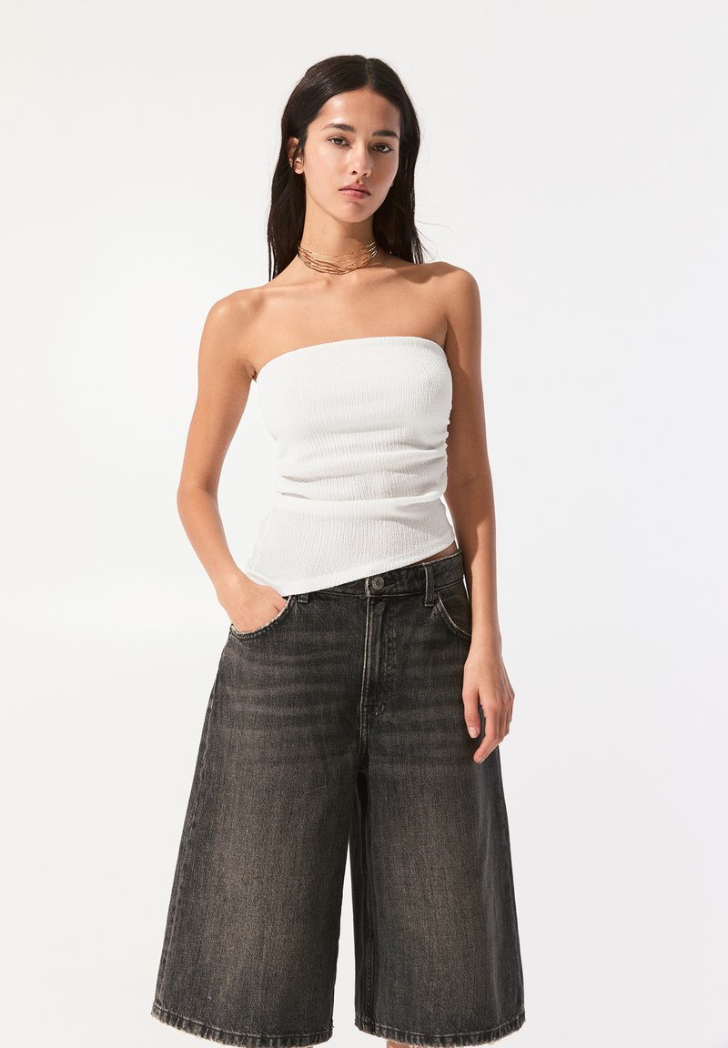 Haut blanc à bretelles sans manches rayé associé à un short en denim foncé à taille haute et jambes larges, avec une texture subtile et des poches avant.