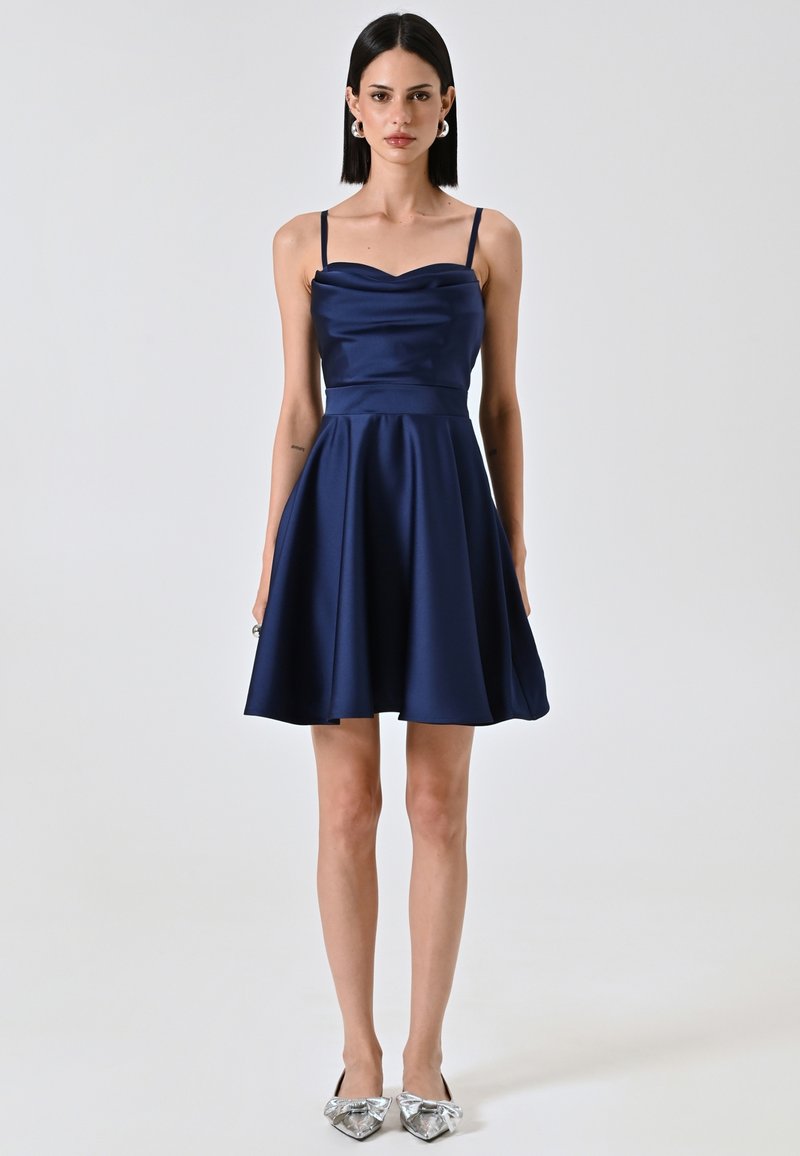 Robe en satin bleu marine avec un décolleté en cœur, des fines bretelles et une jupe évasée. Assortie à des ballerines argentées avec un détail en nœud.