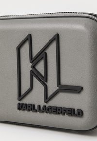 Accessorio grigio texturizzato con logo "KL" in rilievo nero e lettering "KARL LAGERFELD", dotato di zip nera spessa.