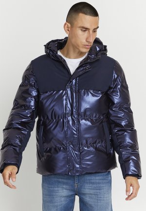 Navy-Blouson mit glänzender Oberfläche, ausgestattet mit einem einfarbigen oberen Abschnitt in Marineblau, Reißverschluss und Druckknöpfen, sowie zwei seitlichen Taschen.
