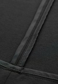 Primer plano de un zipper de tela negra con bordes cosidos y una textura suave y mate en el material circundante.