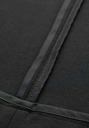 Primer plano de un zipper de tela negra con bordes cosidos y una textura suave y mate en el material circundante.