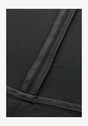 Primo piano di una cerniera in tessuto nero con bordi cuciti e superficie liscia e opaca sul materiale circostante.