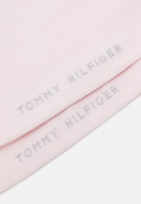 Šviesiai rožinė megzta skara su švelniu tekstūrai, kuri turi atspausdintą tekstą "TOMMY HILFIGER" pilka spalva, esantį arti kraštų.