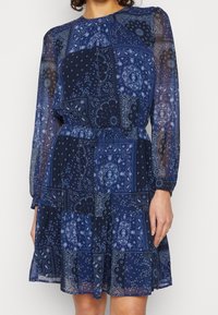 Dunkelblaues Kleid mit langen Ärmeln, das ein Patchwork-Design aus Paisleymustern und Blumenmotiven aufweist. Hergestellt aus transparenter Stoff mit tailliertem Schnitt.