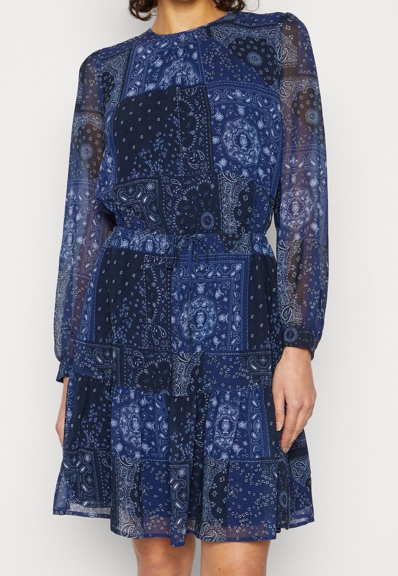 Dunkelblaues Kleid mit langen Ärmeln, das ein Patchwork-Design aus Paisleymustern und Blumenmotiven aufweist. Hergestellt aus transparenter Stoff mit tailliertem Schnitt.