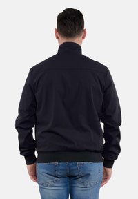 Giacca blu scuro con colletto alto, polsini elastici e vita elasticizzata. Presenta una texture liscia e un design semplice e minimalista.