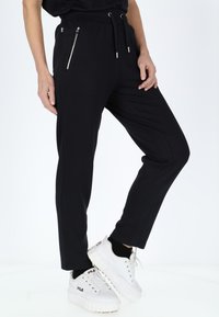 Svarta joggers med dragsko i midjan, dragkedjefickor på sidan och slim fit, tillsammans med vita plattformssneakers.
