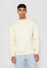 Kremfarget hettegenser med rund hals, lange ermer og ribbede mansjetter, kombinert med lyseblå jeans. Myk tekstur, minimalistisk design.