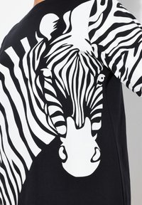Maglietta nera con una grande grafica di zebra bianca, caratterizzata da audaci strisce bianche e nere che evidenziano intricati dettagli delle linee e texture.