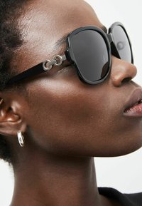 Gafas de sol negras de gran tamaño con acentos circulares plateados en las patillas. Acabado suave y brillante con lentes ahumados.