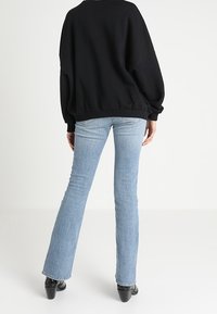 Czarna, oversize bluza z opadającymi ramionami, zestawiona z jasnoniebieskimi spodniami dzwonami i czarnymi botkami na obcasie. Prosty, casualowy wygląd.