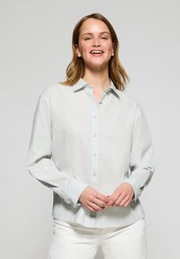 Ljusblå långärmad skjorta med knappslå och subtil textur. Har framknappar och en liten logotyp på bröstet.