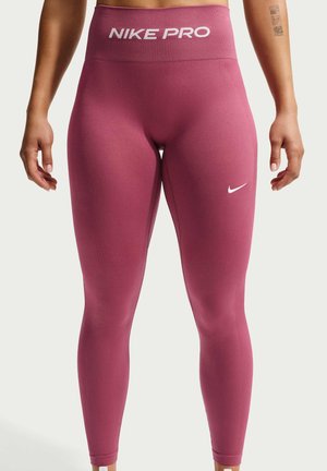 Bordeaux Nike Pro høj-taljede sømløse leggings med hvidt logo på linningen og på det nedre lår, båret af en person, der står mod en ensfarvet baggrund.