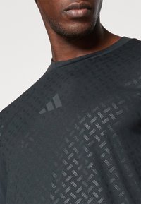 T-shirt de sport noir avec un motif texturé, doté d'un col rond et d'un logo subtil à trois bandes dans des teintes plus sombres sur la poitrine.
