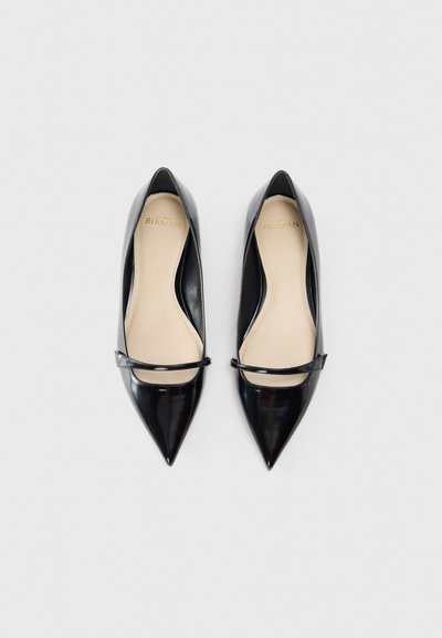 Black patent leather pointed-toe heels with a flat strap across the instep and a beige interior. Smooth texture; sleek design.