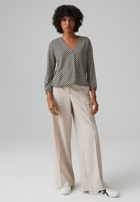 Schwarz-weiße karierte Bluse mit V-Ausschnitt und langen Ärmeln, kombiniert mit hellbeigen weit geschnittenen Hosen und weißen Sneakers.