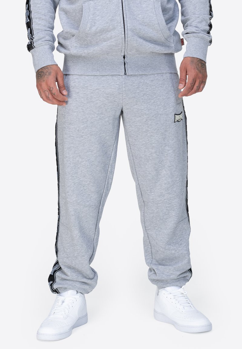Pantalones de chándal grises hechos de una mezcla de algodón, con rayas laterales en negro y acentos de marca, y puños elásticos en los tobillos.