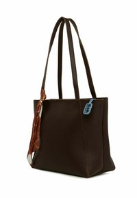 Geantă de umăr din piele maro, cu două mânere, are o eșarfă decorativă legată pe o parte și o etichetă albastră, cusături verticale de-a lungul marginii.