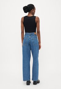 Top nero senza maniche abbinato a jeans in denim blu a vita alta e fit largo. Dettagli notevoli includono tasche posteriori e un'etichetta in pelle in vita.