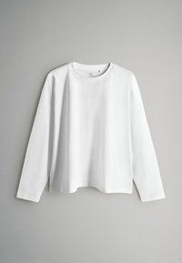 Balti ilgomis rankovėmis medvilniniai marškinėliai, turintys apvalų iškirptę ir laisvą siluetą su nuleistais pečiais bei tiesia apačia.