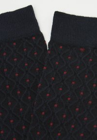 Calcetines de punto azul marino con un patrón de diamantes y pequeños puntos rojos. Los puños son acanalados, lo que proporciona textura y elasticidad adicionales.