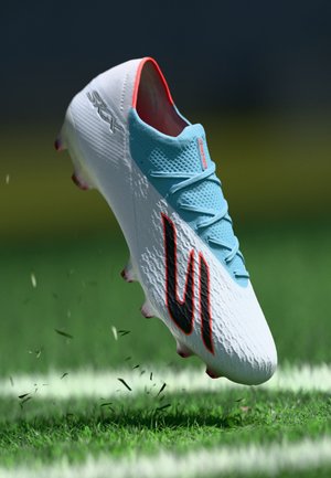 Soccer cleat in white with light blue accents and a black logo, featuring a textured surface and conical studs for traction.