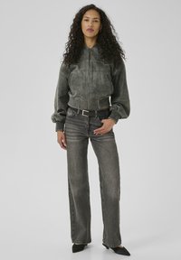Gray leather bomber jacket with ribbed cuffs, paired with high-waisted, faded gray jeans. The outfit features a black belt and pointed black shoes.