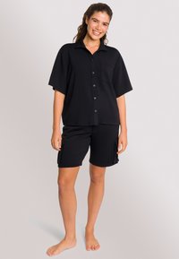 Camicia nera a maniche corte con bottoni, abbinata a pantaloni corti neri con tasche laterali. Tessuto morbido e textured. Design casual.