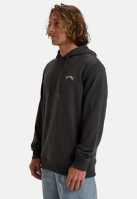 Dark gray hoodie made of soft fabric, featuring a front pocket, drawstring hood, and white logo detail on the chest.