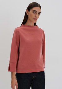 Rosé pink sweatshirt with a high neckline and three-quarter sleeves, featuring pleated detailing at the cuffs, made from soft fabric.