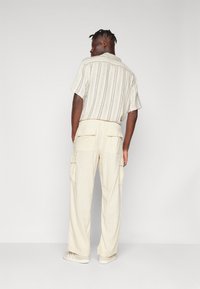 Korte mouwen, gestreept shirt in crème met textuurstof; gecombineerd met crème cargobroek met grote zijzakken en een elastische tailleband.