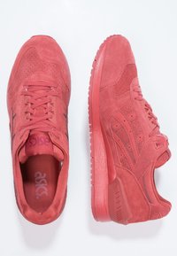 Röda mockaskor för sport med en texturerad yta. Funktioner inkluderar en vadderad krage, snörning fram och framträdande gummisula.