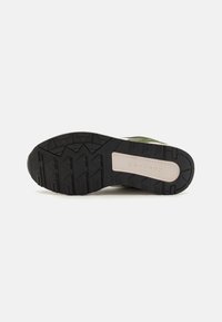 Black rubber outsole with textured grip pattern and beige midsole. Features a green upper with contrasting accents and layered design elements.