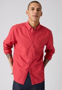 Rode button-up shirt van katoen, met lange mouwen en een opgestikte kraag. Opmerkelijke details zijn een subtiele logo en opgerolde mouwen.