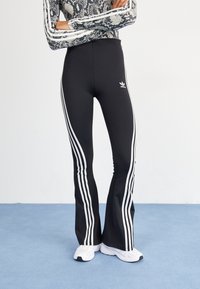 Svarta flare leggings har tre vita vertikala ränder längs sidorna och en liten vit logotyp på framsidan av höften. Snyggt, stretchigt tyg.