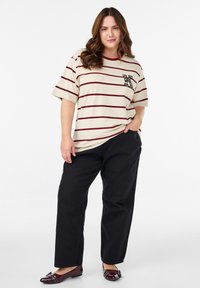 Beige oversized t-shirt with maroon horizontal stripes and a patterned pocket, paired with black wide-leg pants and glossy burgundy loafers.