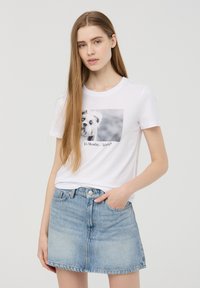 T-shirt bianco in cotone con grafica frontale di un cane e testo "È lunedì... di nuovo?" abbinato a una gonna di jeans azzurri chiari con chiusura a bottoni.