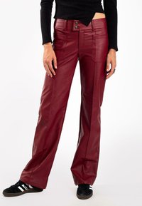 Pantalones anchos de cuero rojo con dos bolsillos frontales y cierre de botón doble. Textura suave y un ajuste a medida. Combinados con zapatillas negras.