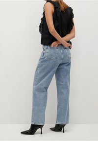 Jeans azzurri a vita alta con vestibilità morbida, dotati di tasche posteriori e orli sfrangiati, abbinati a un top nero con volant e tacchi a punta neri.