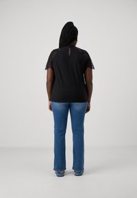 Black top with lace short sleeves and keyhole back detail, paired with blue flared jeans. Smooth fabric, casual fit, clean lines.
