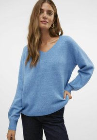 Svetlo modra, mehka, prevelika pulover s V-izrezom in dolgimi rokavi, izdelan iz teksturirane pletenine. V kombinaciji z temnimi kavbojkami.